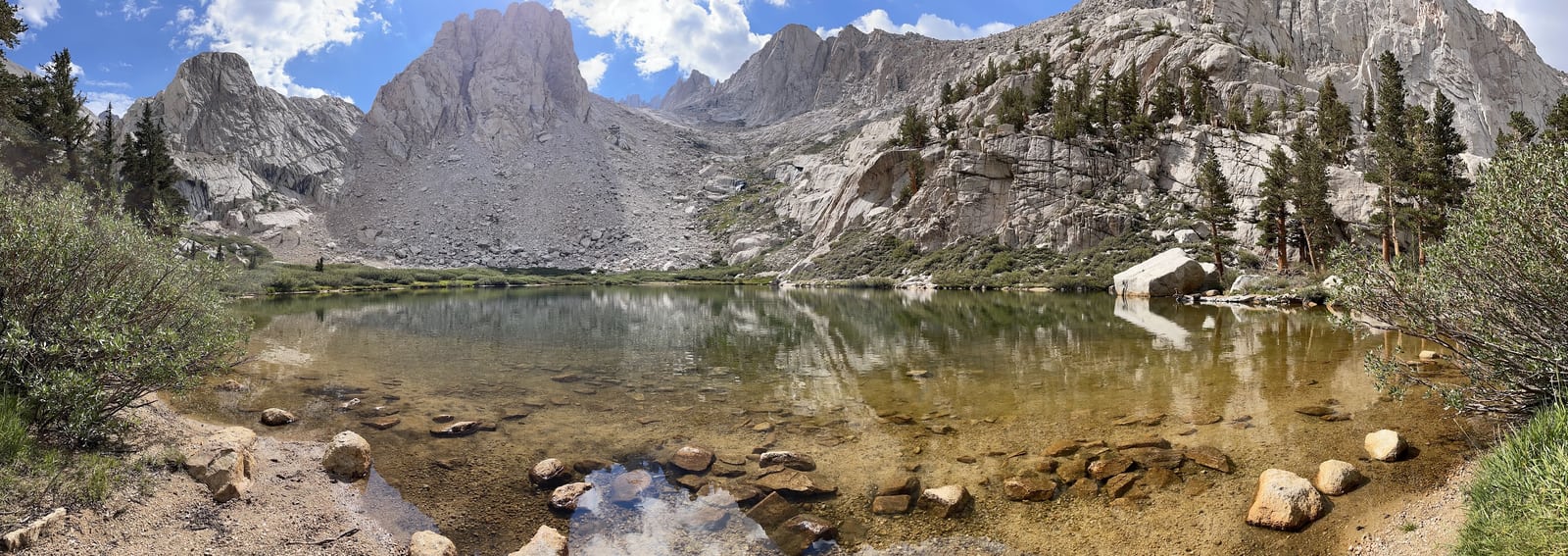 A clear lake beneath pale rocky ridgelines, with pines and rocks along the shore.