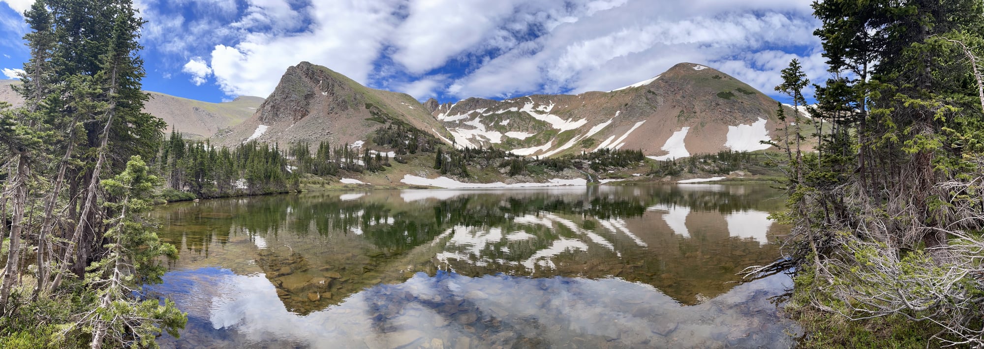 Rocky peaks and pines reflected in a still mountain lake.