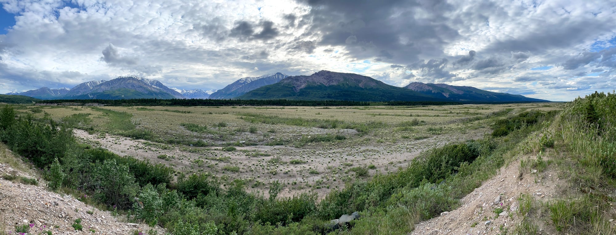 A wide open valley leading to a long line of mountains under heavy clouds.