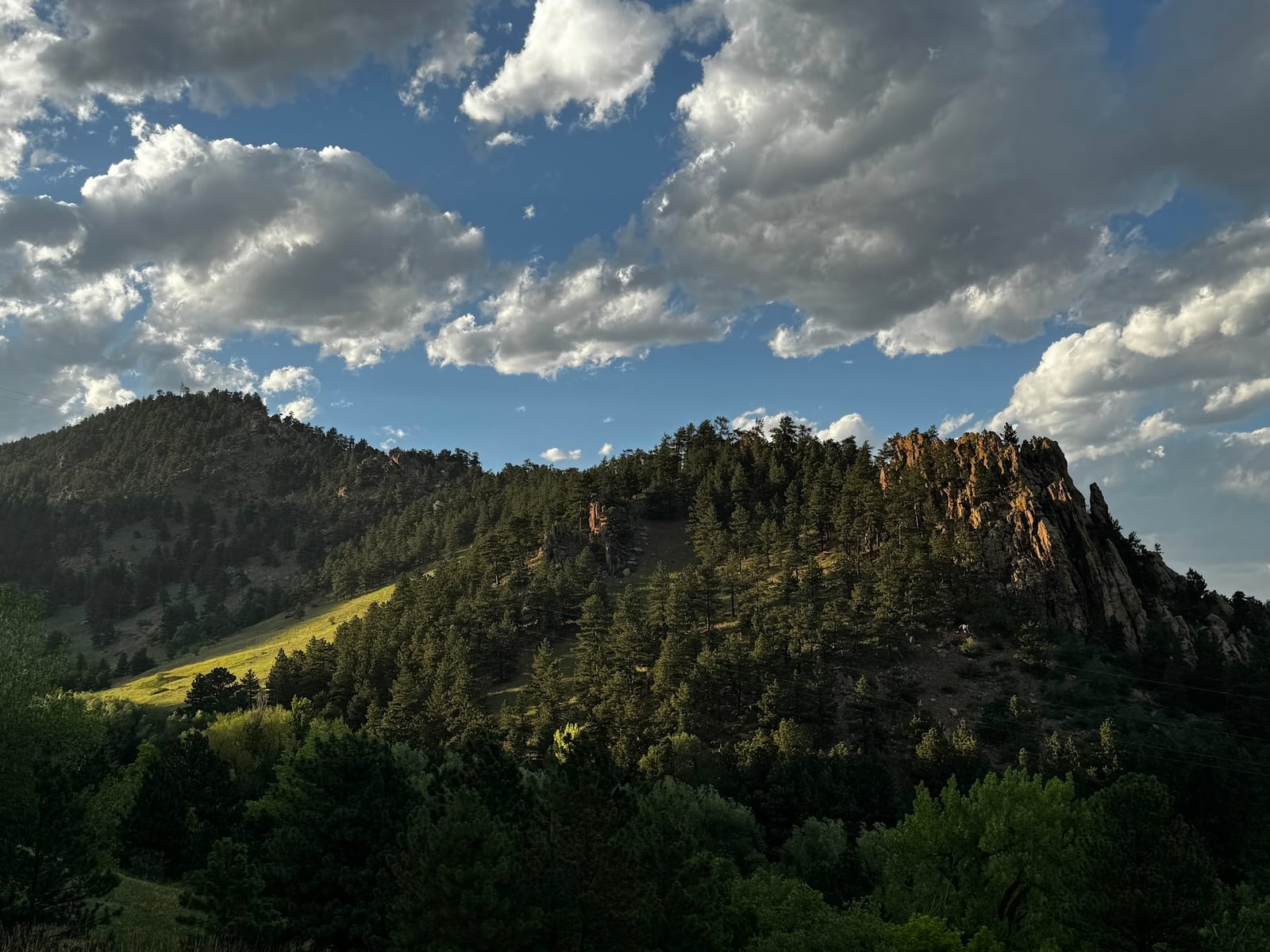 Sunlit clearings on a wooded hillside beneath large clouds and patches of blue sky.